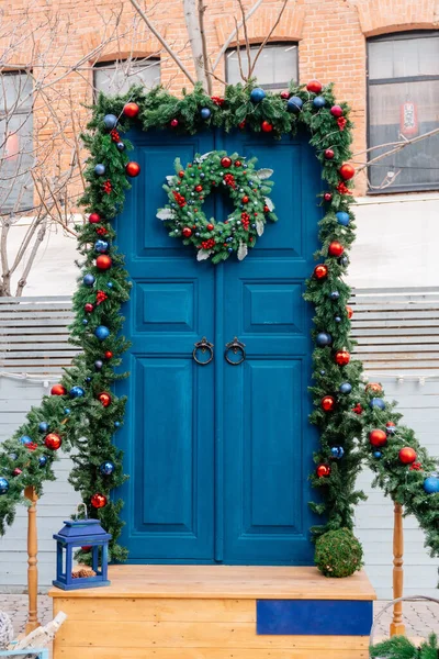 Geleneksel bir Noel çelengi, köknar dalları ve korkuluklarla süslenmiş korkuluklardan oluşan bir Noel çelengi. Mavi kapı, ahşap merdiven, dekoratif fenerler, tahta kutular ve hasır sepetler..