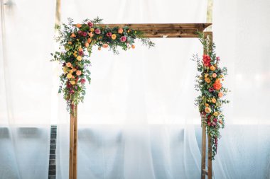 Düğün töreni için ahşap kemer, süslü kumaş, çiçekler ve yeşillik.