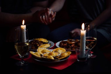 El ele, iki mum, iki bardak şampanya, deniz tarağı, midye ve karides dolu bir tabak kırmızı masa örtüsü.