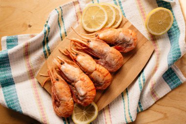 Çizgili bir masa örtüsünün üzerinde tahta bir tahtada botan karidesi ve limon.