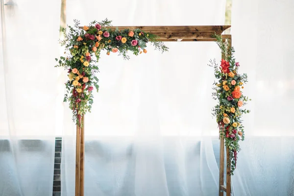 Düğün töreni için ahşap kemer, süslü kumaş, çiçekler ve yeşillik.