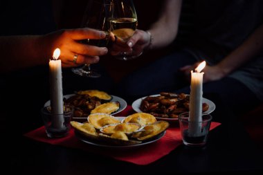 İki şampanya bardağı, iki mum, deniz tarağı, midye ve karides dolu bir tabak kırmızı masa örtüsü.