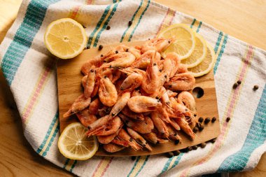 Karides, limon ve biber çizgili bir masa örtüsünde tahta bir tahtanın üzerinde.