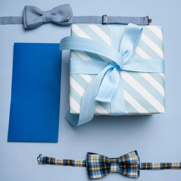 Blue gift box, blue gift envelope and two bow tie on a blue background