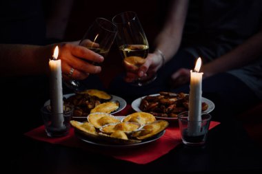 İki şampanya bardağı, iki mum, deniz tarağı, midye ve karides dolu bir tabak kırmızı masa örtüsü.