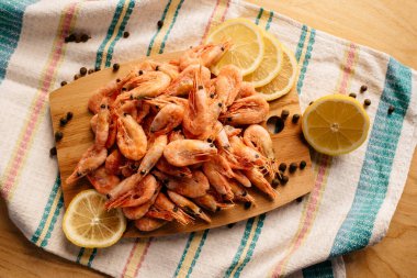 Karides, limon ve biber çizgili bir masa örtüsünde tahta bir tahtanın üzerinde.