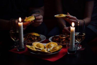 Ellerinde iki deniz tarağı, iki mum, istiridyeli tabaklar, midyeler ve kırmızı masa örtülü karidesler.