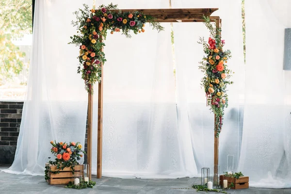 Düğün töreni için ahşap kemer, süslü kumaş, çiçekler ve yeşillik.