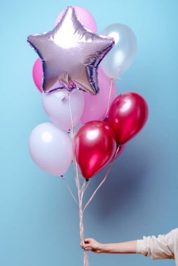 Kırmızı, pembe, şeffaf helyum balonları ve gümüş yıldızlı mavi arka planda bir kadının elinde..