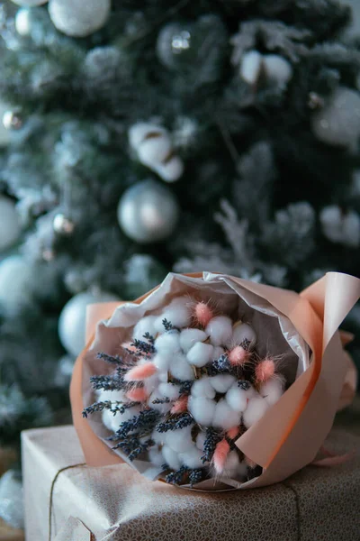 Noel ağacının arka planında el işi kağıda sarılmış şeftali paketinde bir buket çiçek. Cottonwood kutuları, lavanta, lagurular.