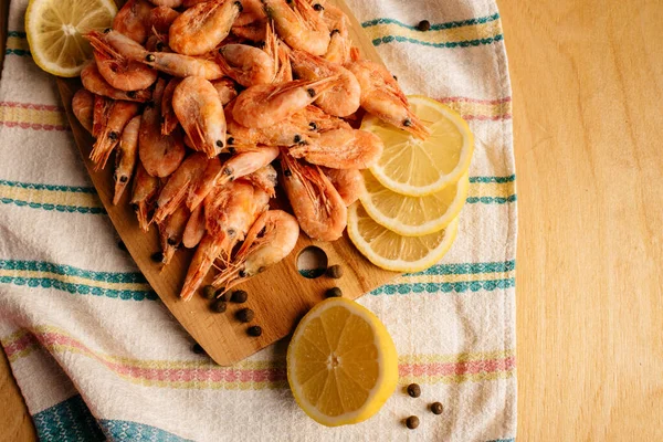 Karides, limon ve biber çizgili bir masa örtüsünde tahta bir tahtanın üzerinde.