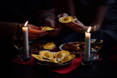 Ellerinde iki deniz tarağı, iki mum, istiridyeli tabaklar, midyeler ve kırmızı masa örtülü karidesler.
