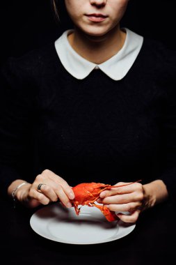 Kız, siyah arka planda beyaz bir tabakta ellerinde kerevit haşladı.