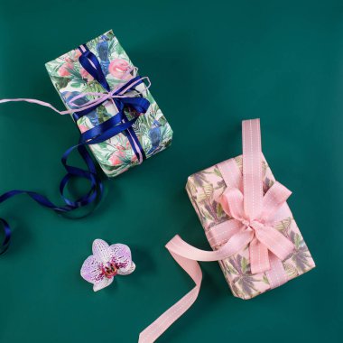 Yeşil arka planda kurdele, ambalaj malzemesi ve orkide ile sarılmış hediye kutusu