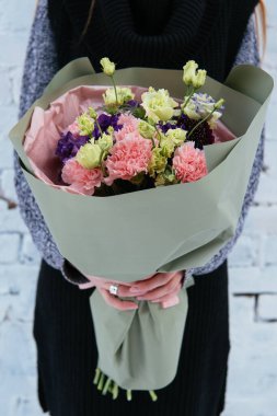 Şam fıstıklı çiçek buketi arka planda örülmüş süveter giyen çiçekçi kadının ellerinde beyaz tuğla duvarda..