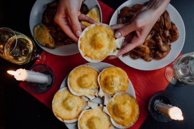 iki bardak şampanya, iki mum, bir kadının ellerinde peynirli istiridye, kırmızı masa örtüsünde beyaz tabaklar, midyeler ve karidesler.
