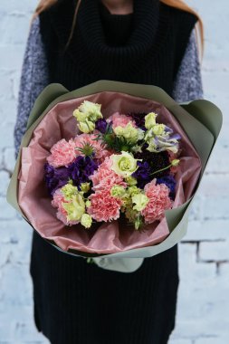 Şam fıstıklı çiçek buketi arka planda örülmüş süveter giyen çiçekçi kadının ellerinde beyaz tuğla duvarda..