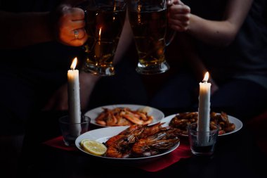 iki el, iki bardak bira, iki mum, karides ve limonlu ıstakoz kırmızı masa örtüsü.