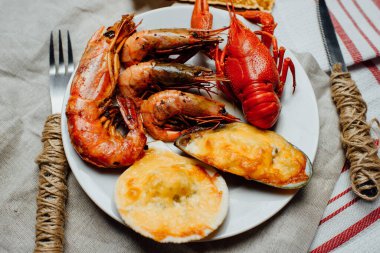 Kaynamış kerevit, fırınlanmış midye ve midye peynirin altında kabuk, kızarmış Langoustines ve karides beyaz bir tabakta çatal ve bıçakla hafif bir arka planda.