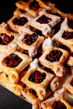 Siyah zemin üzerine pudra şekeri serpiştirilmiş reçelli poğaça.