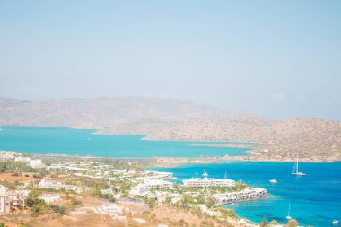 Önünde kayalar ve Kalydon adası ile mavi deniz. Lasithi, Elounda, Yunanistan. Tekneler ile güzel koy.