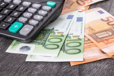 Ekonomi ve bütçe kavramı. Hesap makinesi ve euro parası gri ahşap masada. Tahta zemin üzerinde siyah hesap makinesi olan Euro banknotları. 