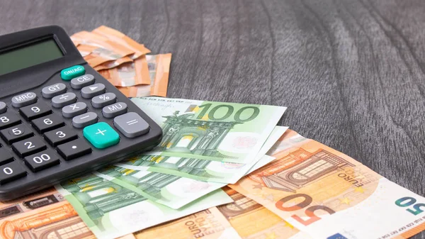 Hesap makinesi ve euro parası gri ahşap masada. Tahta arka planda siyah hesap makinesi olan Euro banknotları. Uzayı metin için kopyala. Mali ve bütçe kavramı.