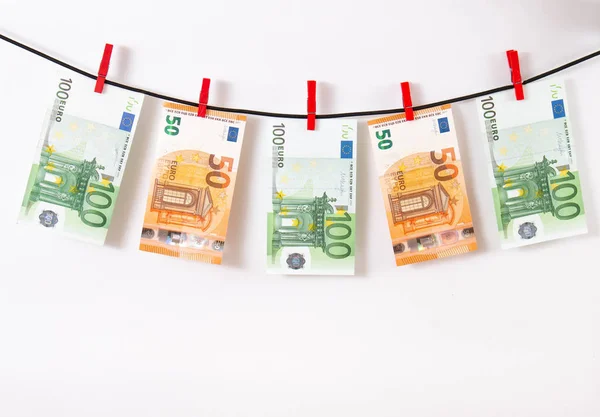 Euro banknotes hanging on a clothesline against white background. Euro money with red clothes pegs on rope. Money Laundering euro hung out to dry. Isolated euro money on string.