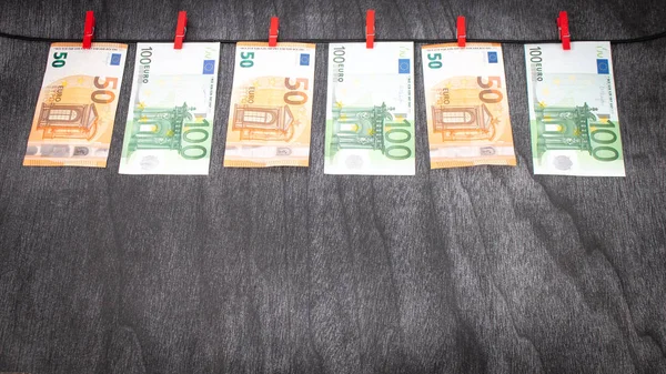 Euro banknotes hanging on a clothesline against grey wooden background. Euro money with red clothes pegs on rope. Money Laundering euro hung out to dry. Euro money on string. Copy space for text.
