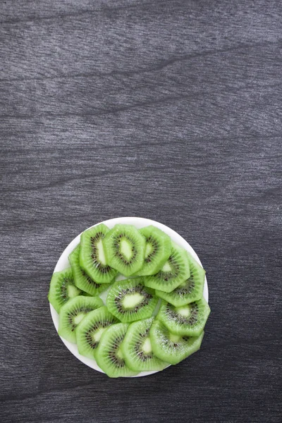 Fresh sliced kiwi on plate. Green Kiwi fruit slices on dark wooden background. Copy space. Kiwi cuted on plate.