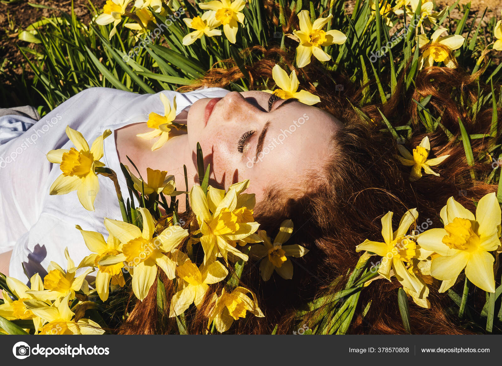 一个红头发的年轻漂亮姑娘躺在水仙上的画像前面的景色春夏快乐的概念 图库照片 C Maksimovat