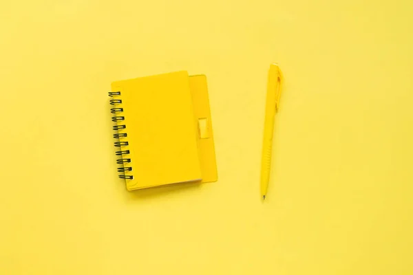 Creative monochrome flat lay of bloggers workspace. Top view of yellow notepad and pen. Yellow background, place for text.