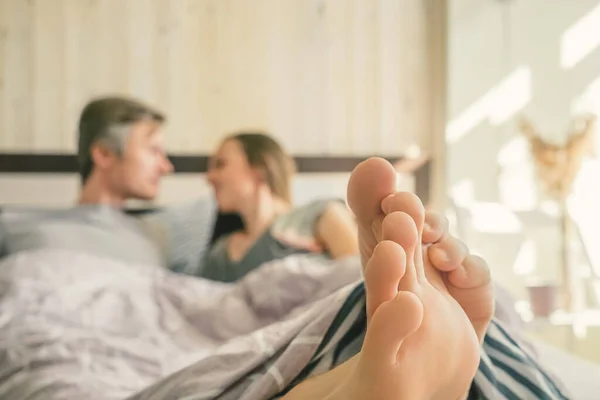 Close-up of the feet of a couple on the bed. Feet on foreground, man and woman on background blurred.