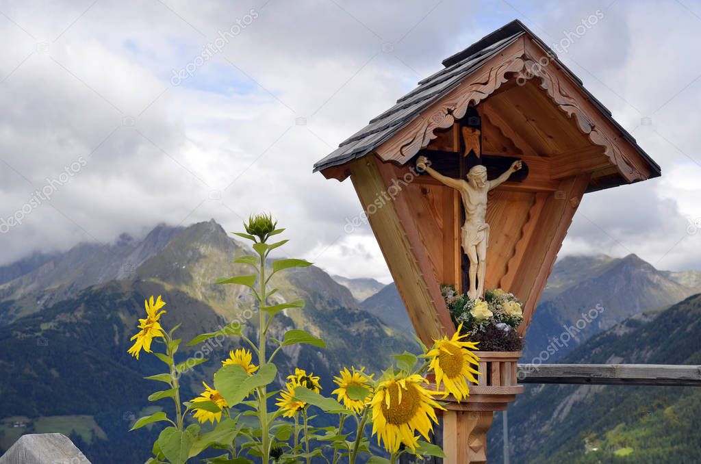 Austria, Tirol, Christian wayside cross and sun flowers on mountain inn in East Tyrol