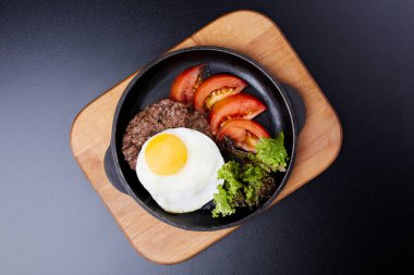 Tavada yumurta, dilimlenmiş domates, salata ve pirzola.