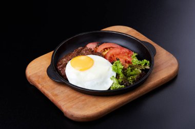 Tavada yumurta, dilimlenmiş domates, salata ve pirzola.