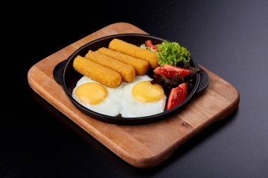 Yakından kızarmış balık çubuğu ya da dökme demir tavada kızarmış balık filetosu. Yağda yumurta, taze domates ve salata..