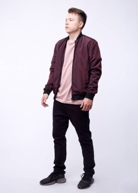 Kot pantolonlu genç adam, beyaz arka planda parlak naylon bordo bombacı ceketi..