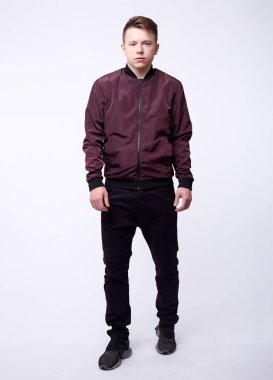 Kot pantolonlu genç adam, beyaz arka planda parlak naylon bordo bombacı ceketi..