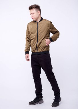 Kot pantolonlu genç bir adam, beyaz arka planda parlak naylon bir bombacı ceketi..