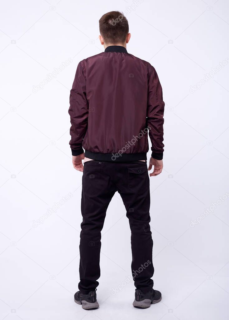 Young man in jeans, shiny nylon burgundy bomber jacket on white background.