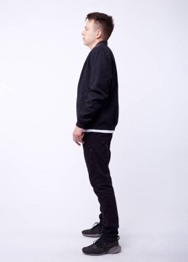 Kot pantolonlu genç adam, beyaz arka planda siyah bombacı ceketi..