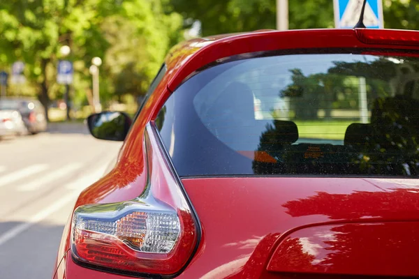 Back window of red car parked on the street in summer sunny day, rear view. Mock-up for sticker or decals