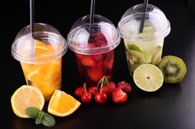 Limonata hazır. Üç bardak nane, kiraz, çilek, kivi, limon, orage, siyah arka planda limon, izole edilmiş.