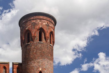 Round brick tower and part of the wall against the blue sky with clouds