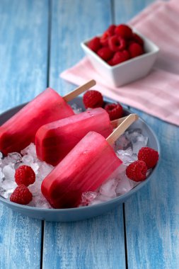 Yanında meyveler olan buzlu ahududu dondurmaları ve daha soğuk hissetmek için mavi ahşap bir arka plan.