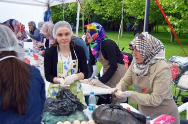 Bükreş, Romanya. 22 Mayıs 2016. Güzel genç kadın kameraya dostça bakarken, Bükreş'teki Türk Festivali'nde Türk kadınlarının geleneksel suberek turtaları için hamur hazırlamalarına yardım ediyor.