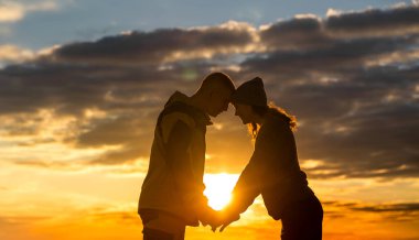 Karantinadan çıktıktan sonra doğa da gün batımını seyreden iki genç insan. Birlikte duruyorlar, el ele tutuşuyorlar, birbirlerine bakıyorlar. Siluetler.