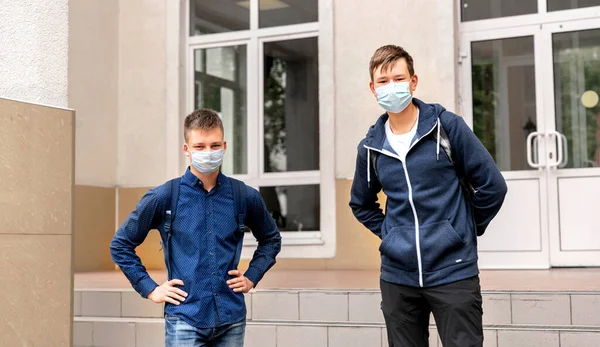 Två skolkamrater står utanför skolan med medicinska masker i ansiktet. — Stockfoto