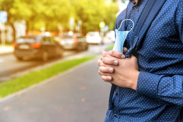 Un adolescente se para en una calle de la ciudad con una máscara médica en sus manos. — Foto de Stock